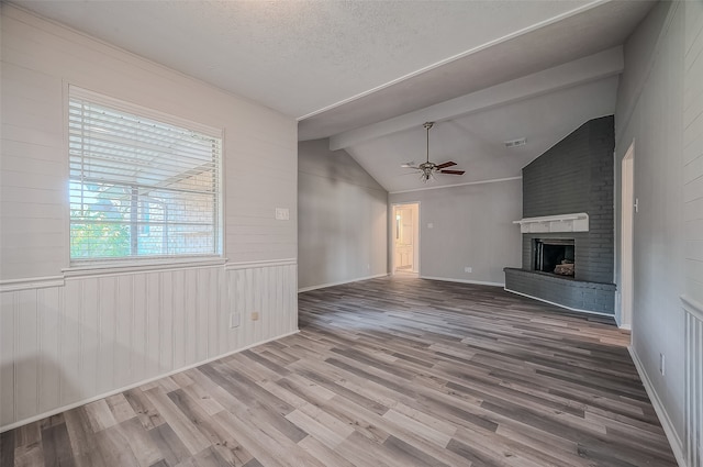 unfurnished living room featuring a textured ceiling, ceiling fan, a fireplace, hardwood / wood-style floors, and vaulted ceiling with beams