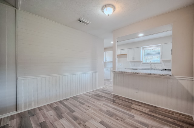 kitchen with sink, tasteful backsplash, wooden walls, white cabinets, and light wood-type flooring