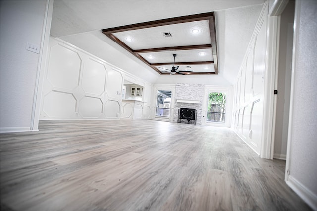 unfurnished living room with beamed ceiling, ornamental molding, ceiling fan, a stone fireplace, and light hardwood / wood-style flooring