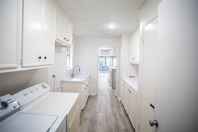 clothes washing area with cabinets, hardwood / wood-style flooring, a textured ceiling, sink, and washing machine and dryer