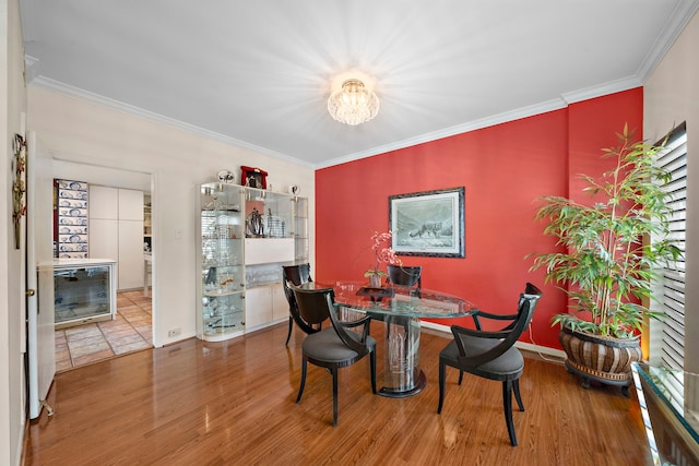 dining area featuring hardwood / wood-style flooring, a notable chandelier, crown molding, and beverage cooler