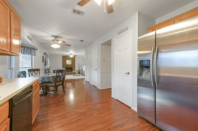 kitchen featuring a brick fireplace, stainless steel appliances, a textured ceiling, dark hardwood / wood-style floors, and ceiling fan