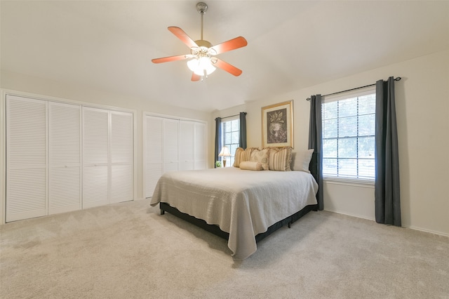 bedroom featuring ceiling fan, multiple windows, light carpet, and two closets