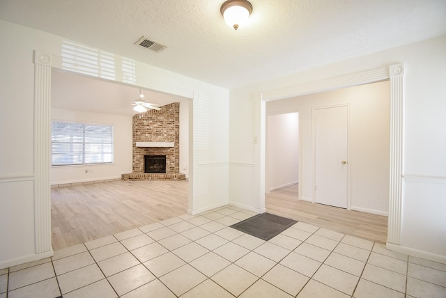 unfurnished living room featuring a textured ceiling, ceiling fan, light hardwood / wood-style floors, and a fireplace