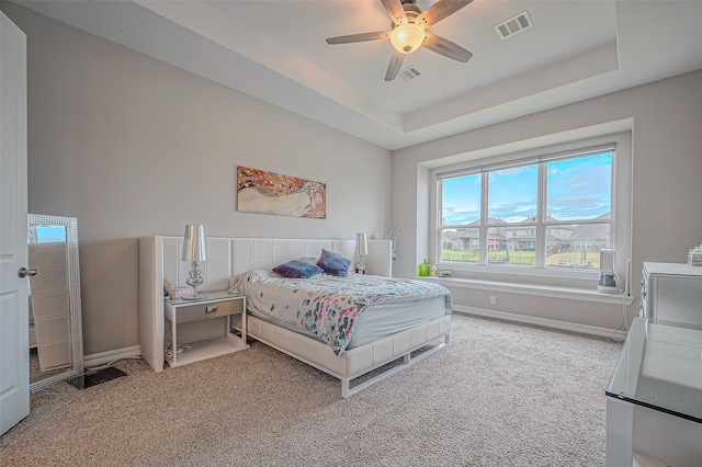 carpeted bedroom with ceiling fan and a raised ceiling