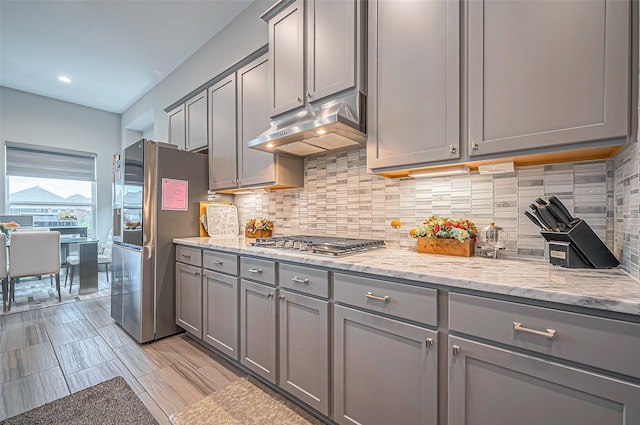 kitchen with stainless steel appliances, gray cabinets, light stone countertops, and decorative backsplash