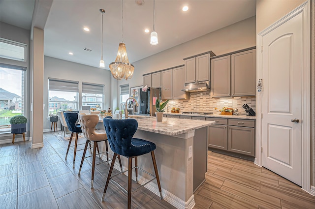 kitchen with a kitchen breakfast bar, gray cabinetry, decorative light fixtures, and an island with sink