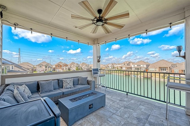 view of patio / terrace with an outdoor living space with a fire pit, a water view, ceiling fan, and a balcony