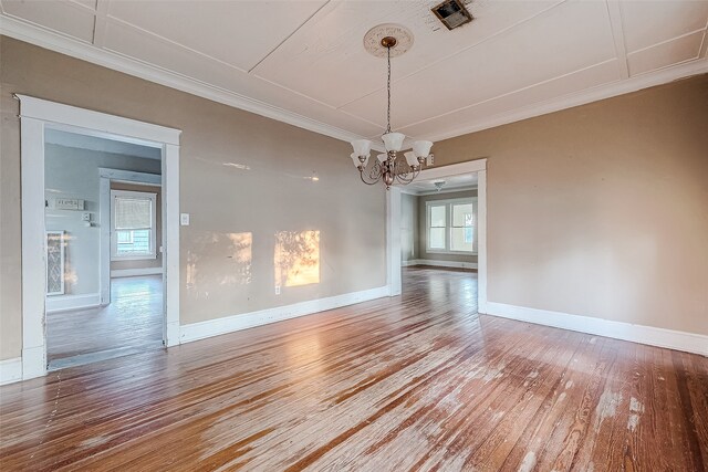 unfurnished dining area with hardwood / wood-style floors, crown molding, and a notable chandelier