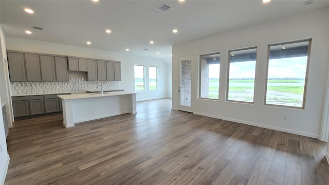 kitchen featuring backsplash, sink, hardwood / wood-style flooring, gray cabinets, and an island with sink