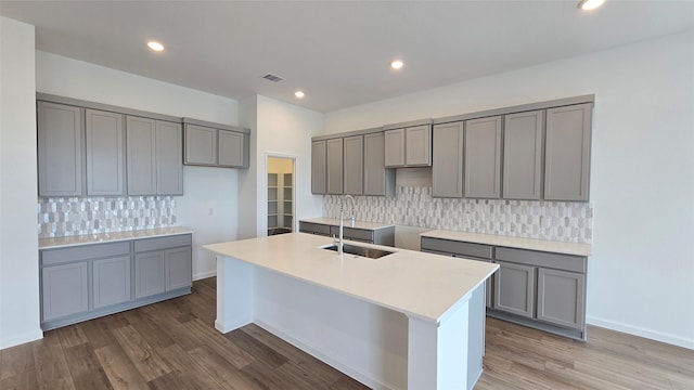 kitchen featuring backsplash, gray cabinetry, a kitchen island with sink, sink, and hardwood / wood-style floors