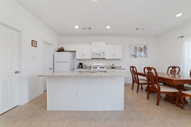 kitchen featuring a center island with sink, light stone counters, white cabinets, light tile patterned flooring, and white appliances