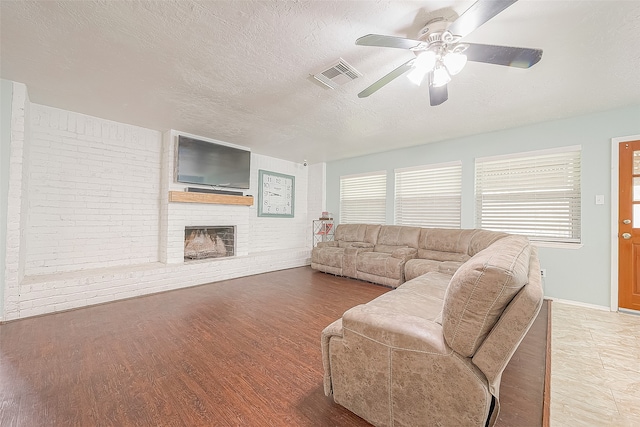 living room with a textured ceiling, hardwood / wood-style flooring, ceiling fan, and a fireplace