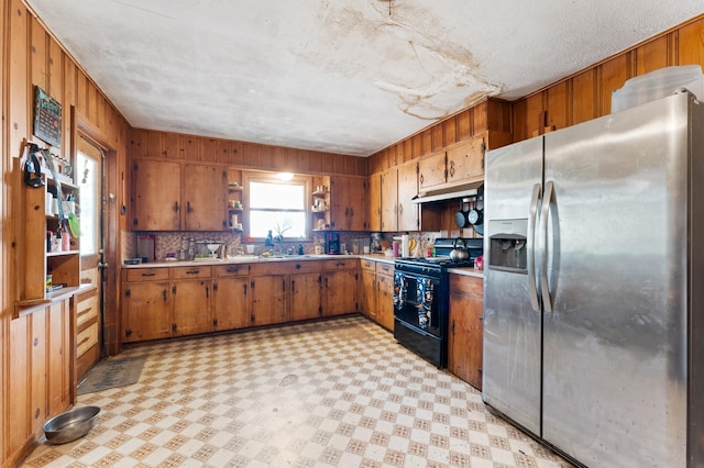 kitchen featuring decorative backsplash, black / electric stove, wood walls, a textured ceiling, and stainless steel fridge