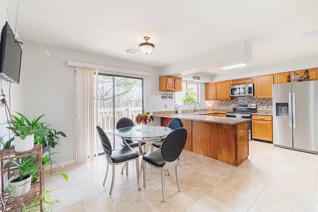 kitchen featuring light stone countertops, tasteful backsplash, kitchen peninsula, light tile patterned flooring, and appliances with stainless steel finishes