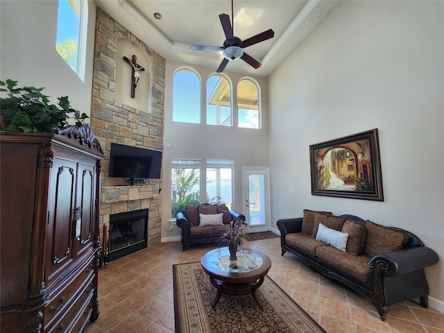 tiled living room featuring a high ceiling, ceiling fan, a stone fireplace, and a healthy amount of sunlight