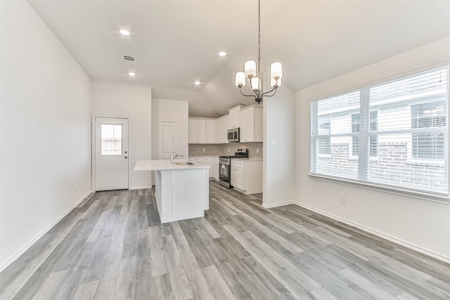 kitchen with a center island with sink, appliances with stainless steel finishes, lofted ceiling, white cabinets, and light wood-type flooring