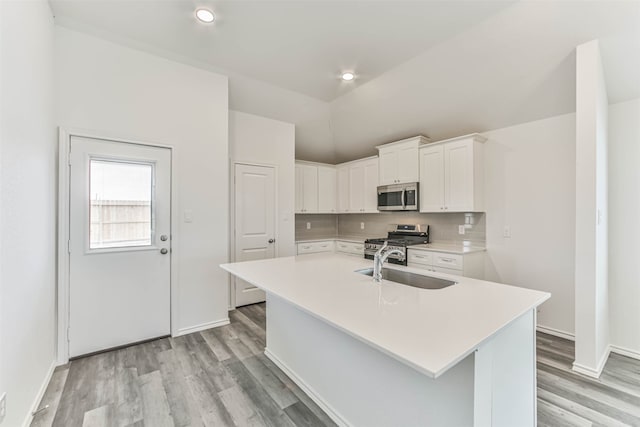 kitchen with a center island with sink, appliances with stainless steel finishes, tasteful backsplash, white cabinets, and light wood-type flooring