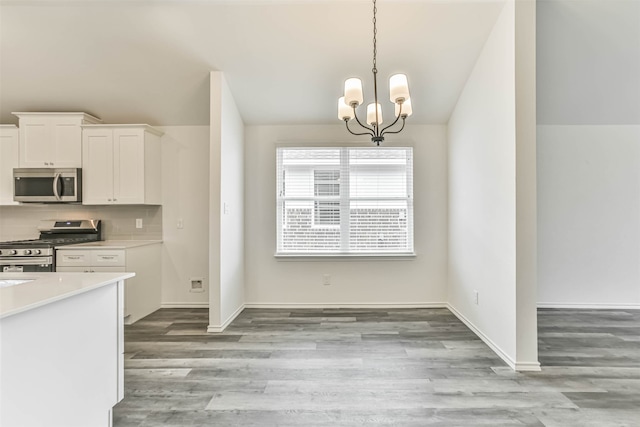 kitchen with stainless steel appliances, light wood-type flooring, white cabinetry, backsplash, and an inviting chandelier