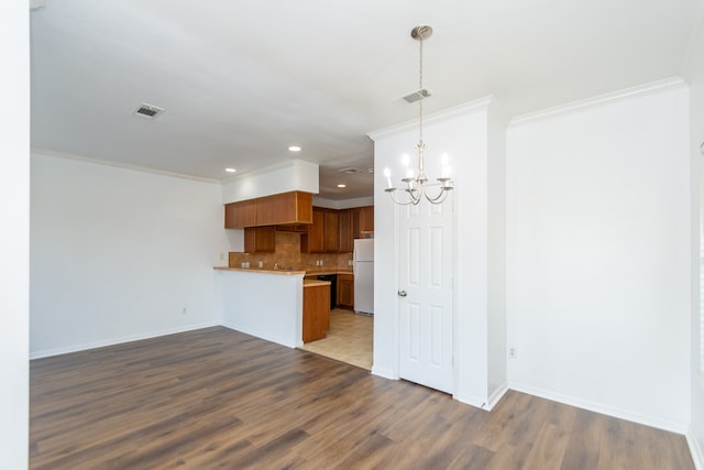 kitchen with wood-type flooring, white fridge, crown molding, decorative backsplash, and kitchen peninsula