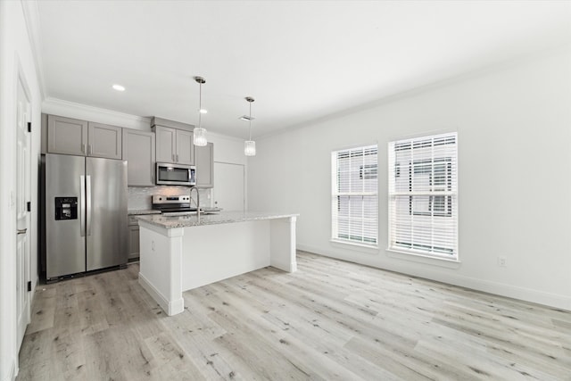 kitchen with stainless steel appliances, a center island with sink, light stone counters, gray cabinets, and light wood-type flooring