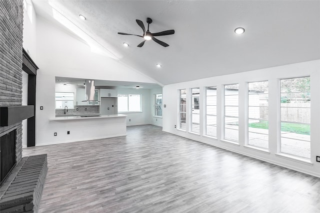 unfurnished living room with high vaulted ceiling, wood finished floors, a ceiling fan, baseboards, and a brick fireplace