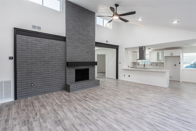 unfurnished living room with light hardwood / wood-style flooring, high vaulted ceiling, a brick fireplace, ceiling fan, and brick wall