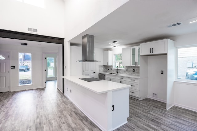 kitchen featuring light hardwood / wood-style floors, white cabinetry, sink, backsplash, and wall chimney range hood