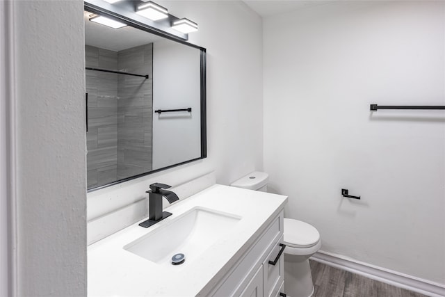 bathroom featuring toilet, vanity, wood-type flooring, and tiled shower