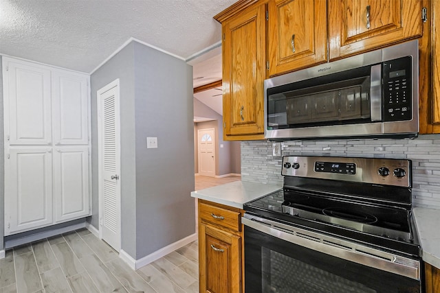 kitchen featuring a textured ceiling, backsplash, appliances with stainless steel finishes, and ornamental molding