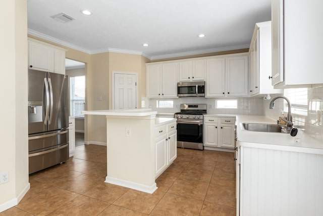 kitchen with appliances with stainless steel finishes, light tile patterned floors, sink, white cabinets, and a center island