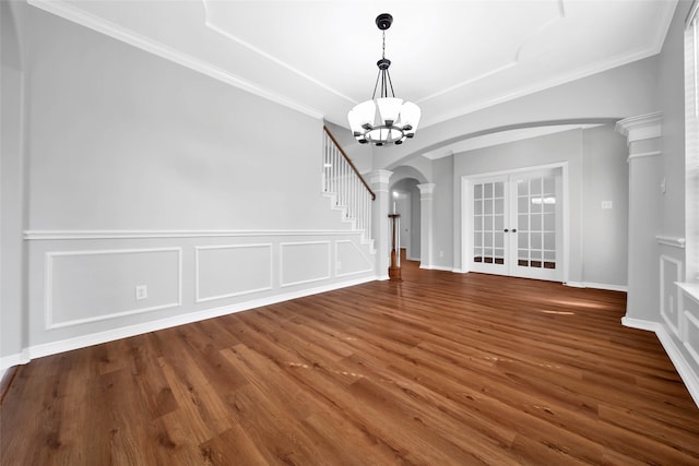 unfurnished dining area with ornate columns, dark hardwood / wood-style flooring, crown molding, an inviting chandelier, and french doors