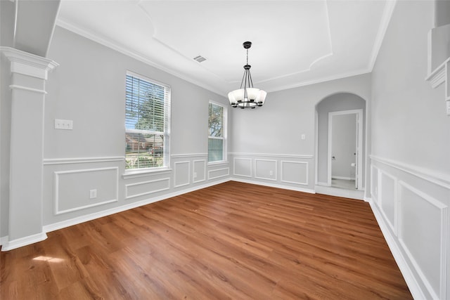 unfurnished dining area featuring an inviting chandelier, wood-type flooring, crown molding, and ornate columns