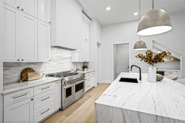 kitchen with decorative light fixtures, double oven range, sink, and an island with sink