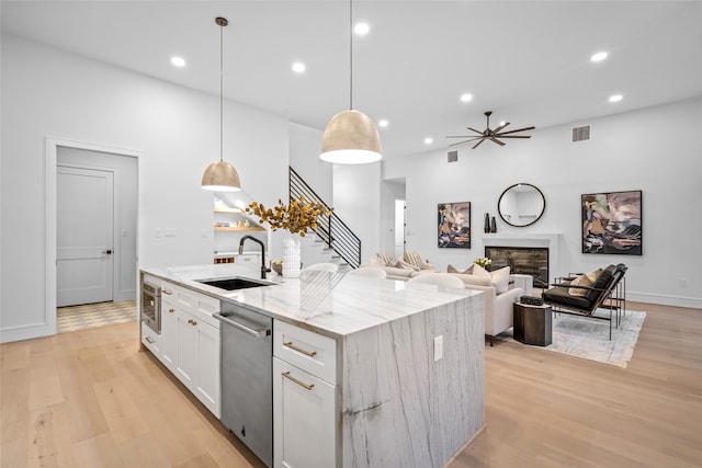 kitchen with a center island with sink, sink, decorative light fixtures, light hardwood / wood-style flooring, and white cabinets