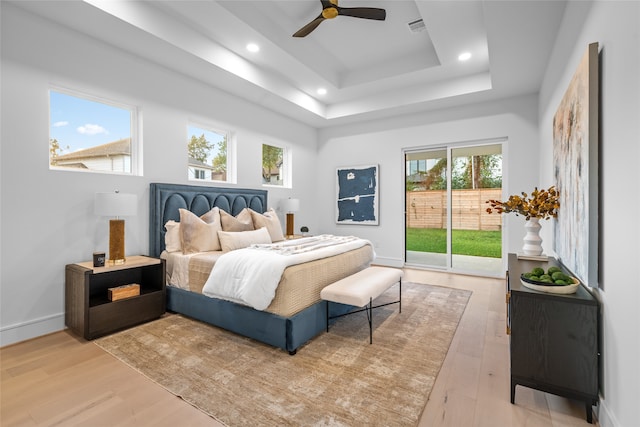 bedroom with access to outside, light wood-type flooring, a tray ceiling, and ceiling fan