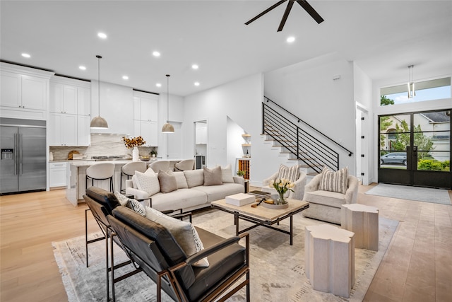 living room with light wood-type flooring, ceiling fan, and a high ceiling