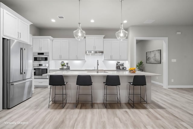 kitchen featuring stainless steel appliances, a breakfast bar, decorative light fixtures, an island with sink, and white cabinets