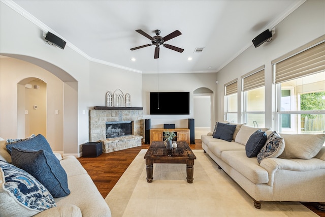 living room with light wood-type flooring, a stone fireplace, ceiling fan, and crown molding