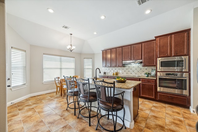 kitchen featuring decorative backsplash, stainless steel appliances, vaulted ceiling, a kitchen island with sink, and decorative light fixtures