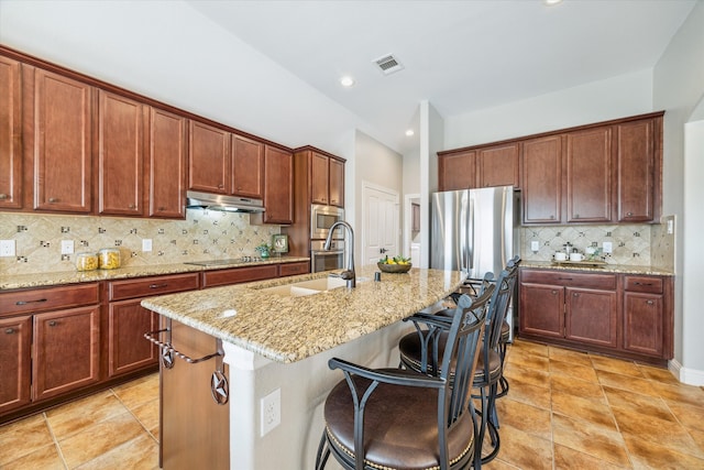 kitchen featuring light stone countertops, appliances with stainless steel finishes, backsplash, sink, and an island with sink