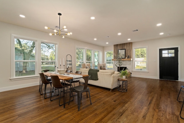 dining room with dark hardwood / wood-style floors, a healthy amount of sunlight, a large fireplace, and a notable chandelier