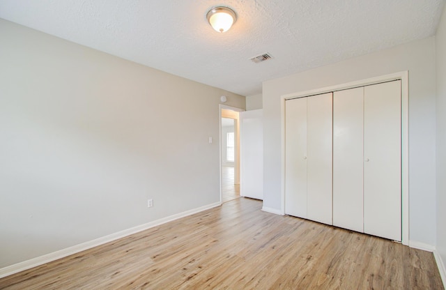 unfurnished bedroom featuring a textured ceiling, light wood-type flooring, and a closet