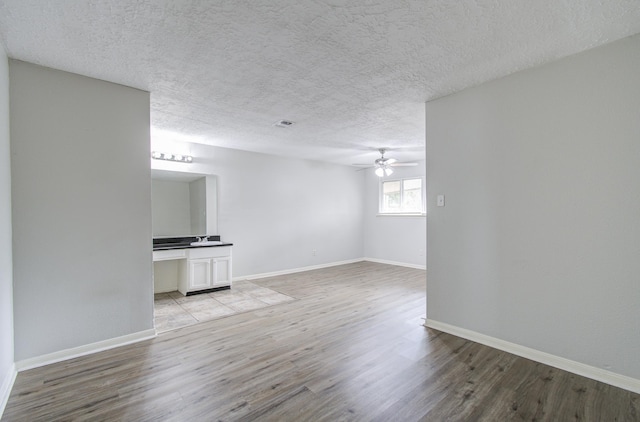 unfurnished room with ceiling fan, sink, light wood-type flooring, and a textured ceiling