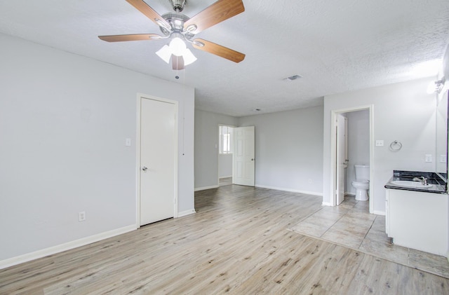 unfurnished room featuring ceiling fan, sink, light hardwood / wood-style floors, and a textured ceiling