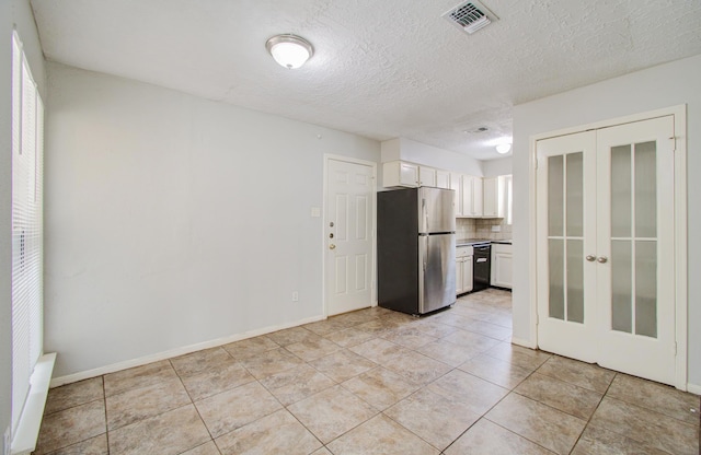 kitchen featuring black dishwasher, tasteful backsplash, light tile patterned flooring, stainless steel fridge, and white cabinets