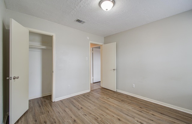 unfurnished bedroom featuring a textured ceiling, light hardwood / wood-style flooring, and a closet