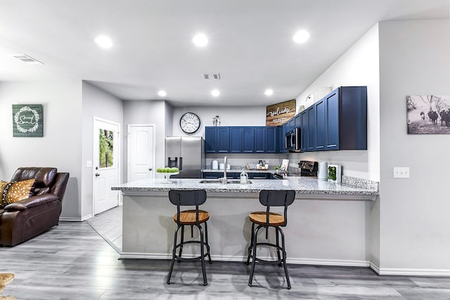 kitchen with stainless steel appliances, a kitchen bar, light hardwood / wood-style floors, blue cabinets, and kitchen peninsula