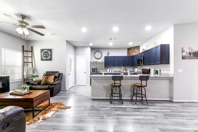 kitchen featuring kitchen peninsula, light hardwood / wood-style flooring, a breakfast bar area, blue cabinetry, and appliances with stainless steel finishes