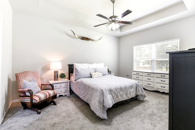 bedroom with light carpet, ceiling fan, and a raised ceiling